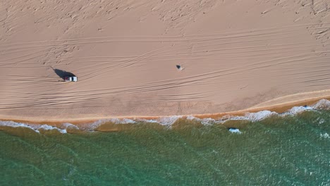 aerial view of a vehicle driving on a sandy beach next to turquoise ocean waves. stunning coastal landscape.