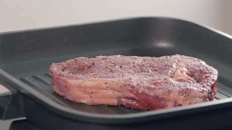 slow motion shot of adding a ribeye steak to a hot griddle pan