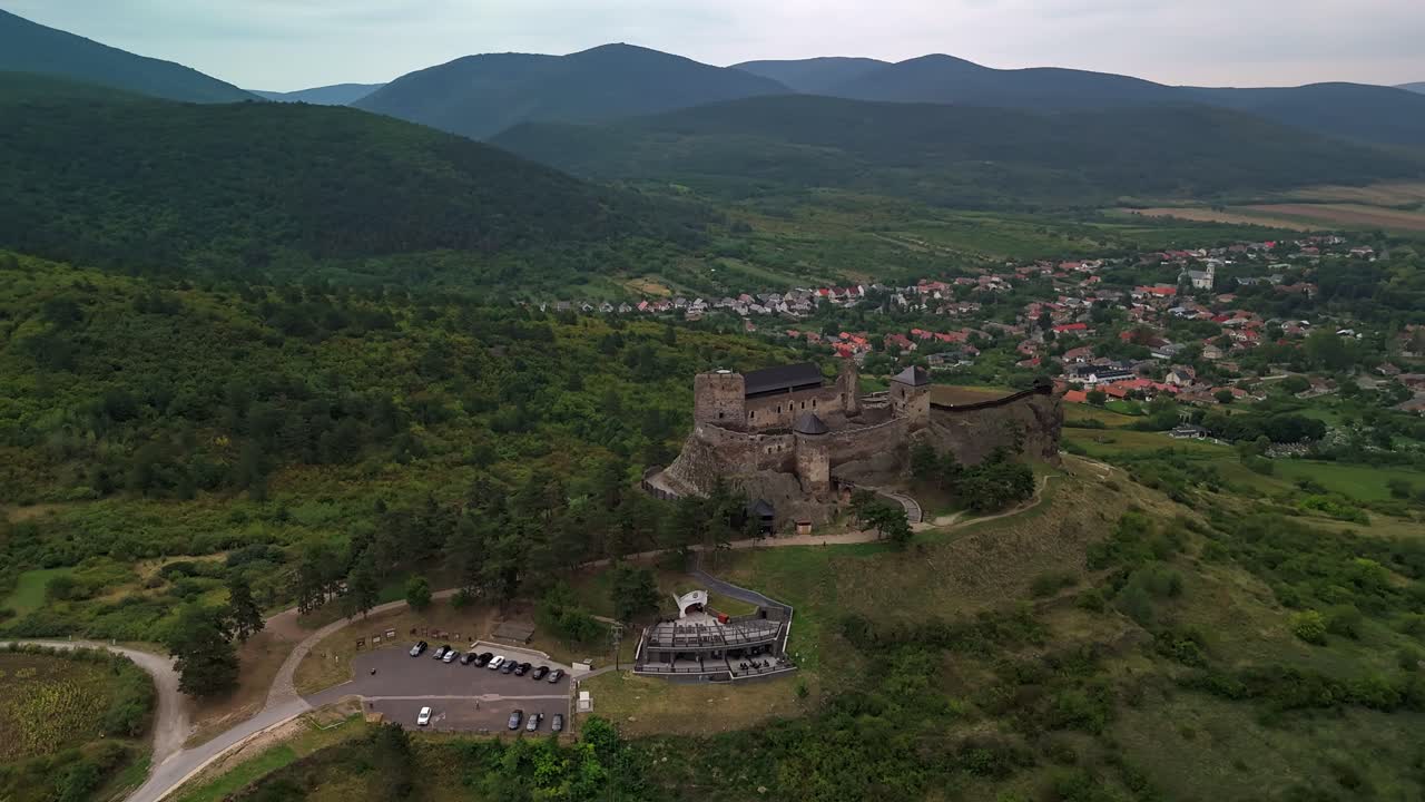 Orbiting drone view of Boldogkőváralja Castle, a medieval landmark nestled among lush greenery, hills and a small village in Hungary, showcasing its historic architecture and picturesque surroundings