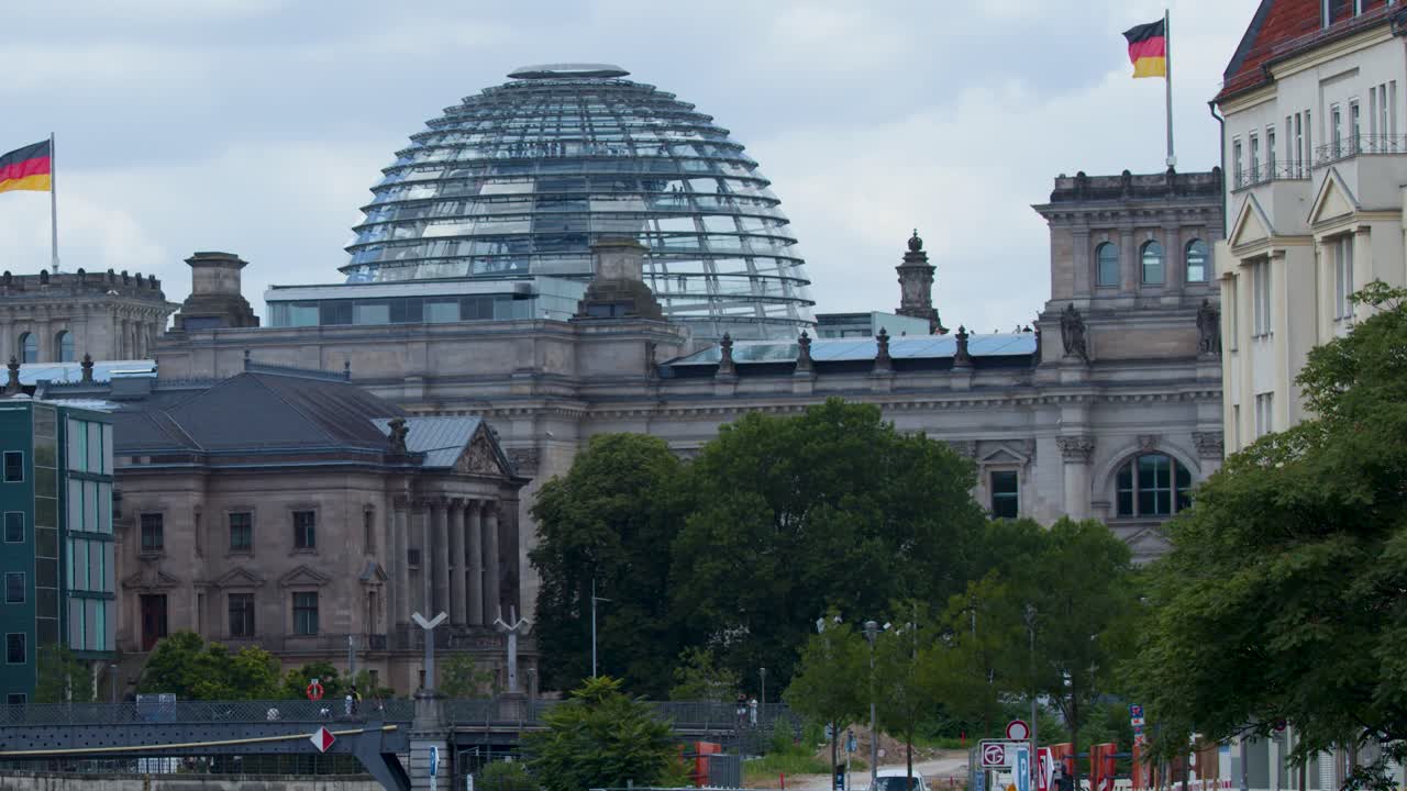 Camera glides along river, revealing Reichstag dome, modern offices, cloudy sky, and cityscape