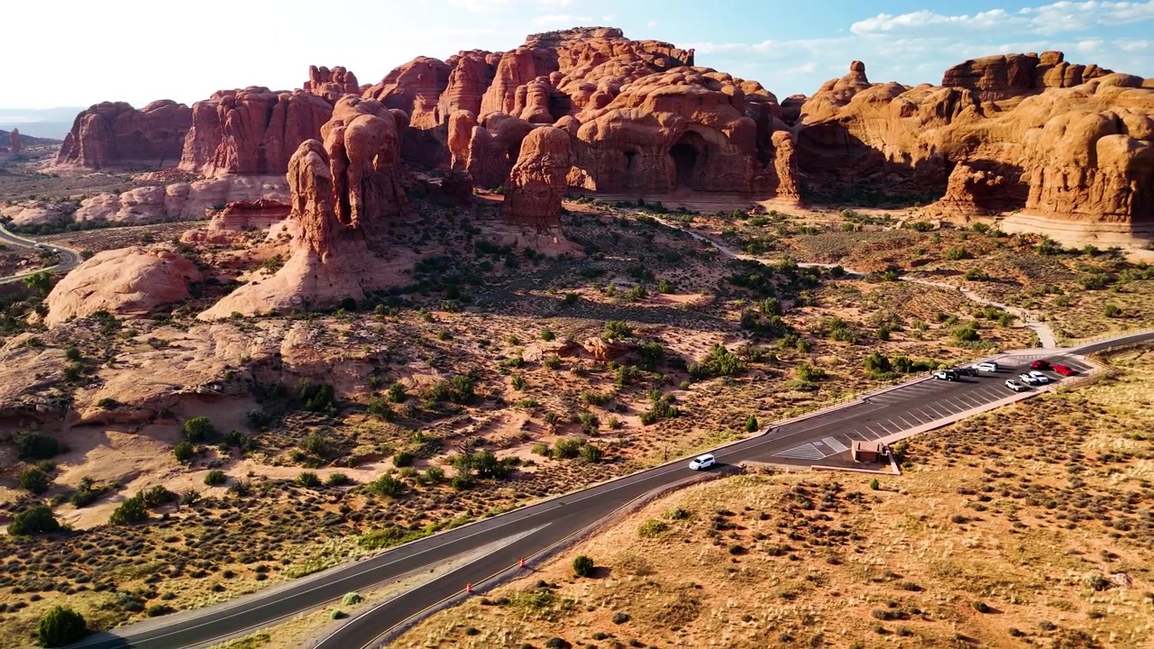 Splendido filmato stock del Parco Nazionale di Arches, USA, durante un pomeriggio luminoso. La luce solare brillante illumina le maestose strutture di arenaria rossa e il paesaggio desertico sotto un cielo azzurro limpido.