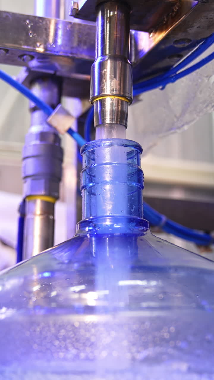 Clean water is filling the big blue bottle from a metal tube. Water overflows the flask. Close up. Vertical video