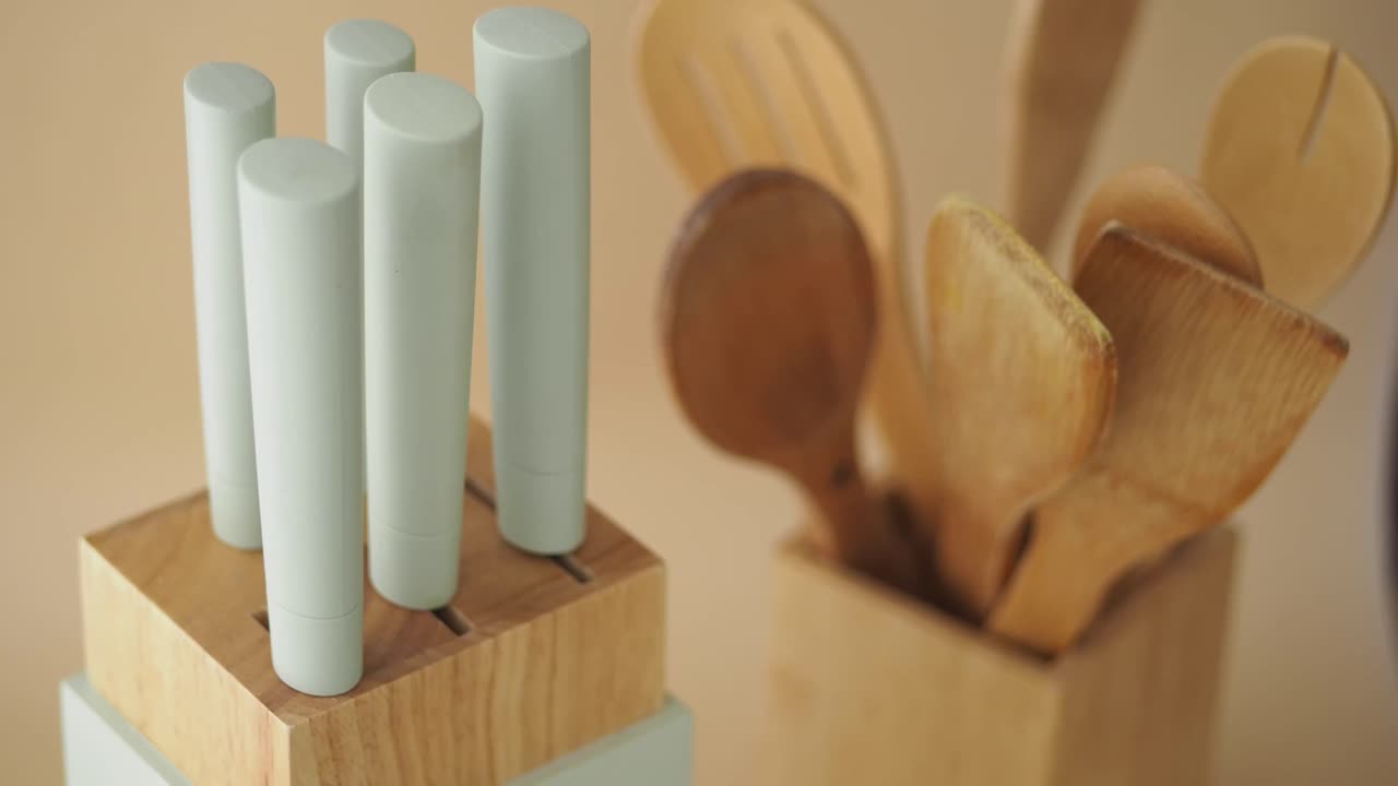 Ceppo con coltelli da cucina e utensili in legno su sfondo beige