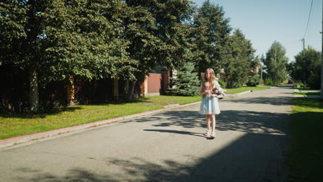 young girl in light blue dress walks alone along quiet neighborhood street under tree shadows, holding stuffed animal with thoughtful expression in peaceful daytime suburban setting