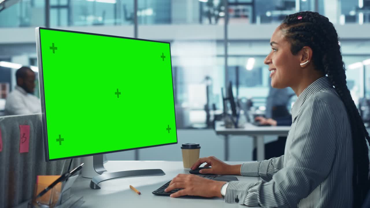Ufficio aziendale diversificato: Bella tecnica IT donna di colore che usa un computer desktop con schermo Chroma Key verde. Ingegnere del software creativo lavora su marketing e sviluppo di progetti eCommerce