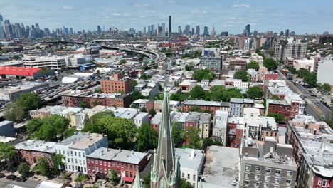 aerial orbiting shot of church tower in brooklyn district with waterfront and magnificent skyline of new york city in background at sunny day - establishing drone shot