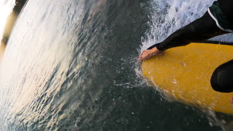 Primer-Plano-De-Una-Tabla-De-Surf-Amarilla-Con-Las-Piernas-De-Un-Hombre-Mientras-Navega-En-Mui-Ne,-Vietnam-Durante-El-Día