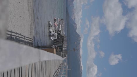 Ein-Ruhiger-Holzsteg-Und-Boote-Auf-Einem-See-Mit-Bergen-Und-Wolken-Im-Hintergrund