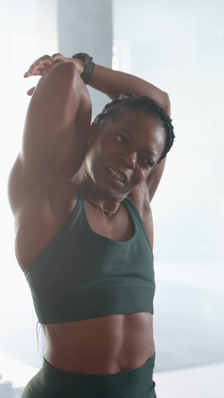 Vertical video: African American woman in sports bra warming up, stretching arm for studio workout
