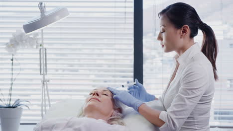 beautician giving mature female patient botox injection in forehead