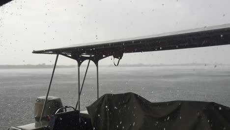 A-huge-rain-downpour-falls-over-the-Chobe-river-in-Kasane,-Botswana-during-a-hot-summers-with-a-boat-in-the-foreground