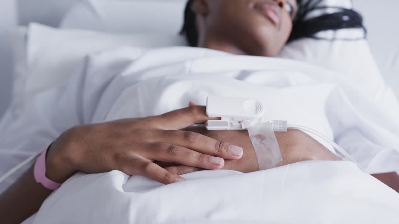 Mani di paziente afroamericana sdraiata a letto in una stanza d'ospedale, al rallentatore.