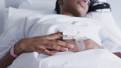 hands of african american female patient lying in bed in hospital room, slow motion