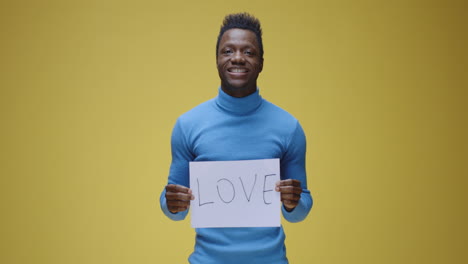 smiling black man holding "love" sign against yellow background