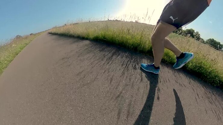 Telecamera ravvicinata immersiva a seguire con movimento vorticoso, angolazioni e prospettive mutevoli, che mostra un trail runner uomo su un argine di valle in pianura alluvionale.