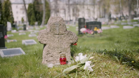 cross tombstone with a white flower and a grave candle on the grass in a graveyard on a sunny day