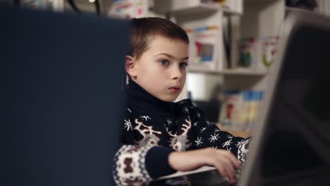 Portait-footage-of-a-little-boy-wth-big-blue-eyes-trying-to-learn-how-to-use-laptop.-Educational-process.