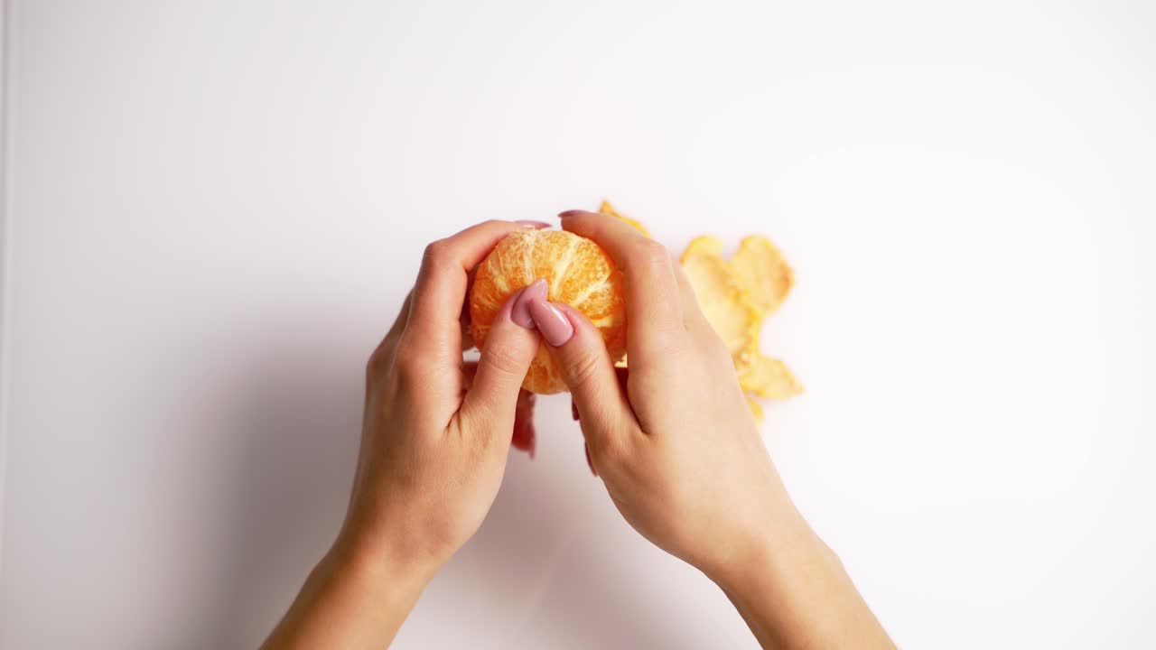 Process of clearance the mandarin. Female's hands cleaning an orange fresh fruit on white background. Top view.