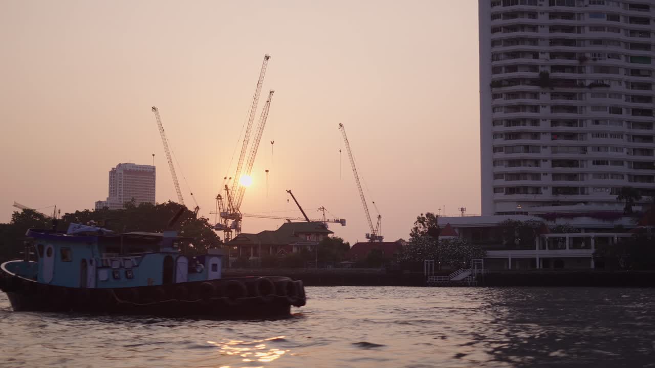 Sunset View of a River with Boats, City, and Construction Cranes