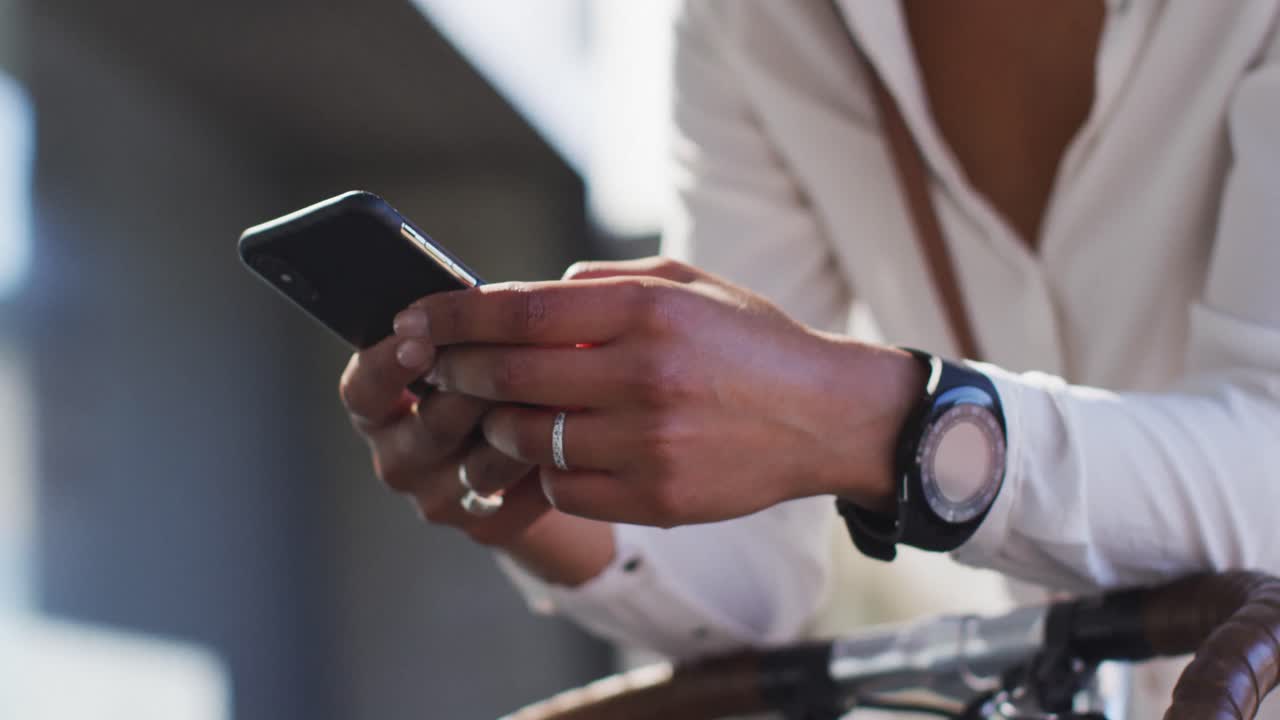 Midsection of african american woman using smartphone leaning on bike in street