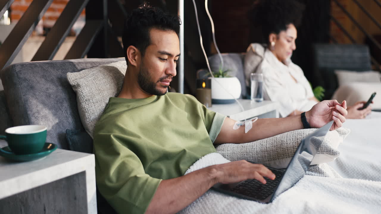 Man with IV Drip Working on Laptop While Recovering at Home