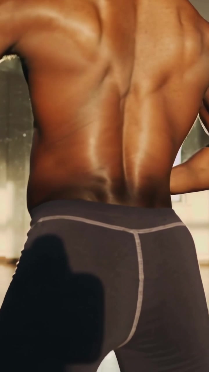 Video verticale: Uomo che ruota, spostando il peso, girandosi in studio vicino a una finestra e aggiustando la posa in pantaloncini.