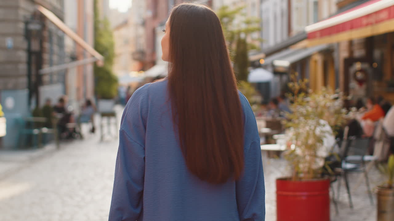 Rear view of young woman tourist walking through the street outdoors looking searching for a way