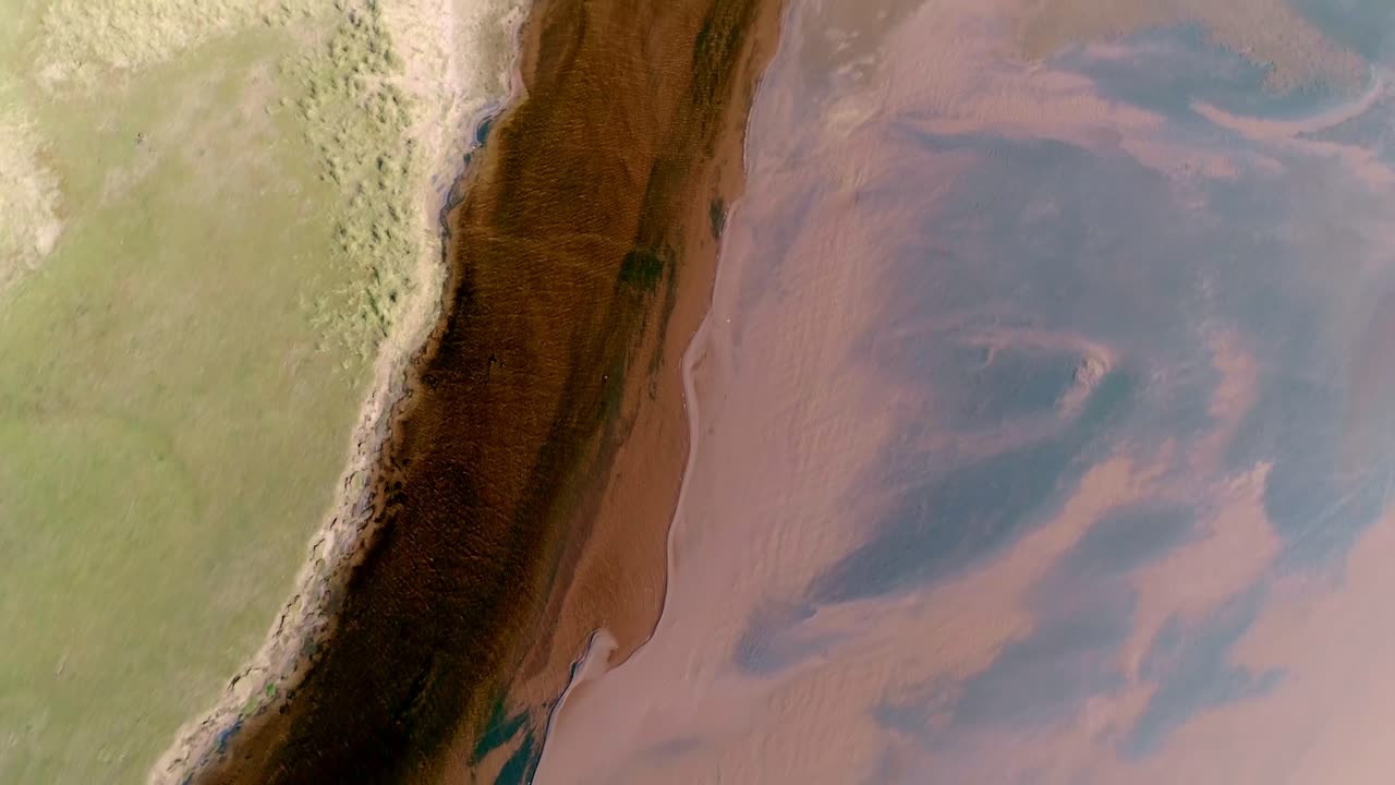 de arriba hacia abajo de un río de color oscuro contrastante tallado entre una duna de arena y un lado de hierba y un banco de arena de color rojo limo