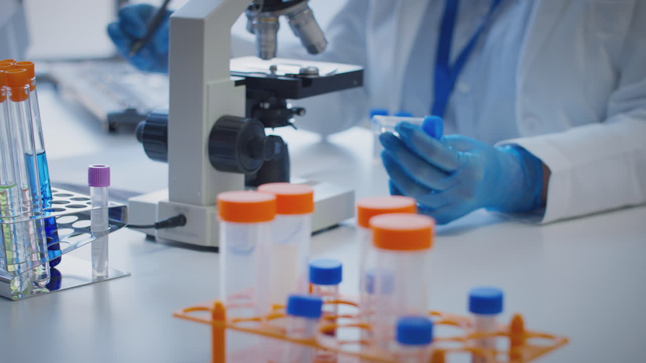 primer plano de un trabajador de laboratorio que realiza investigaciones utilizando un microscopio sosteniendo un tubo de ensayo etiquetado mu