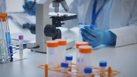 Close-Up-Of-Lab-Worker-Conducting-Research-Using-Microscope-Holding-Test-Tube-Labelled-Mu