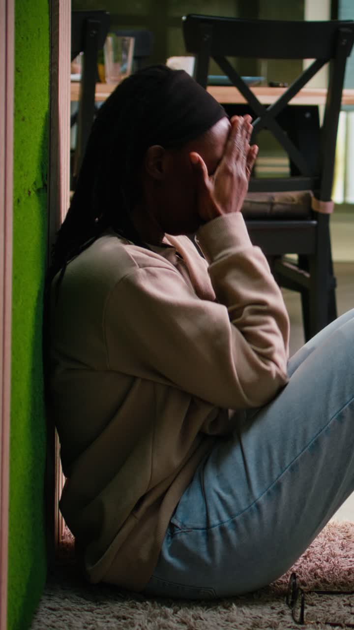 Vídeo Vertical Mulher negra, em crise de saúde mental, sentada no chão, com o coração partido