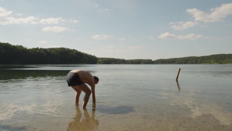 hombre sin camisa está tirando piedras en el lago de jezioro glebokie en polonia