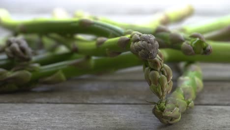 Aufnahmen-Von-Einem-Bund-Frischer,-Grüner-Spargel,-Der-Auf-Einen-Holztisch-Fällt