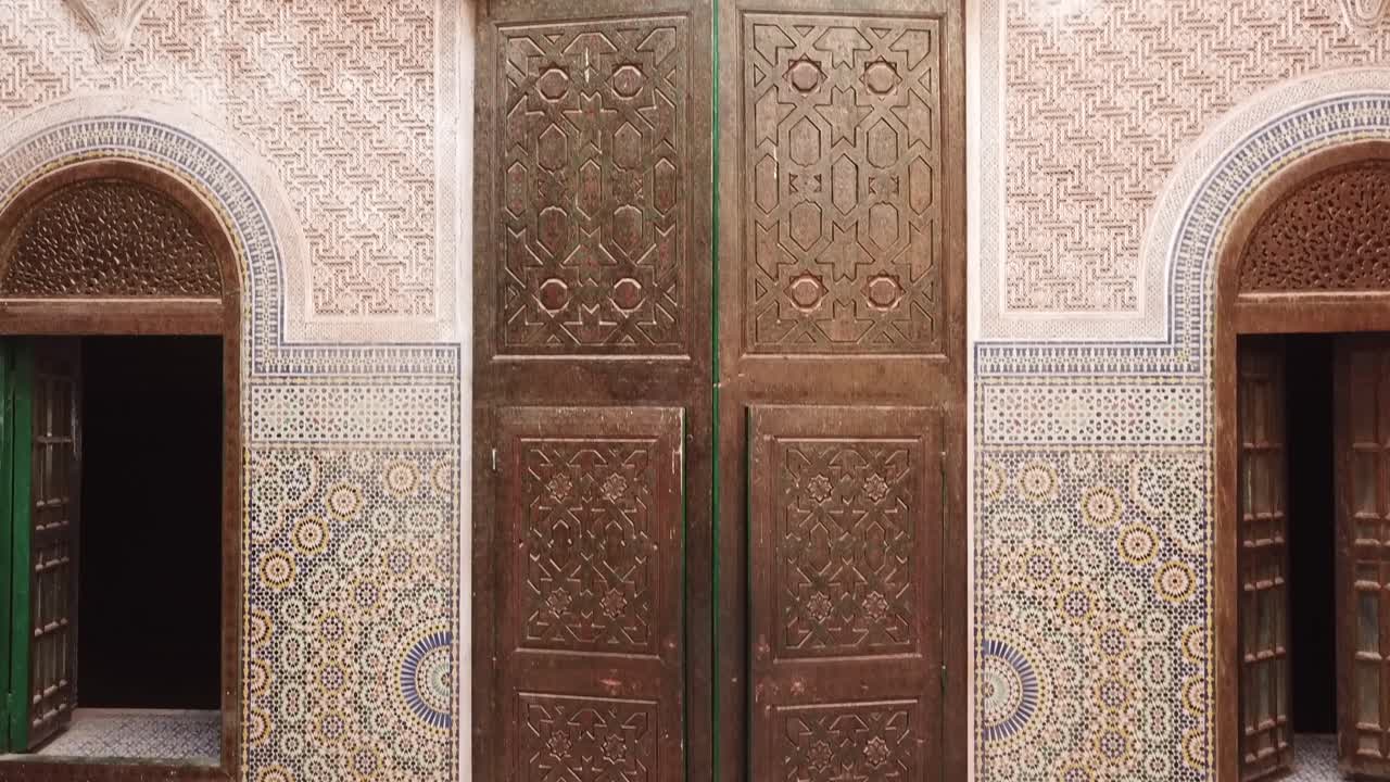 Close view of a traditional Moroccan wooden door surrounded by intricate zellige tile patterns. Rich geometric design and craftsmanship ideal for culture, architecture, and design visuals
