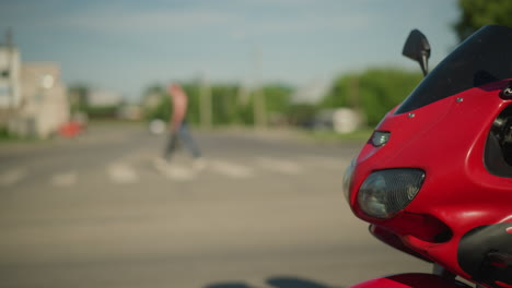 a female motorcyclist wearing a blue checkered top and gloves is riding a red power bike with another rider holding onto the tank from behind, with a blur view of people and cars on