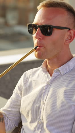 young man having relaxing time resting in hookah bar. male in sunglasses smoking shisha close up. blurred backdrop. vertical video
