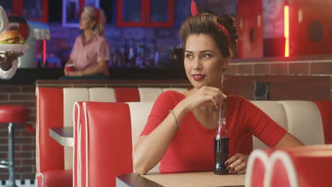 waiter serves a burger to a smiling rockabilly woman