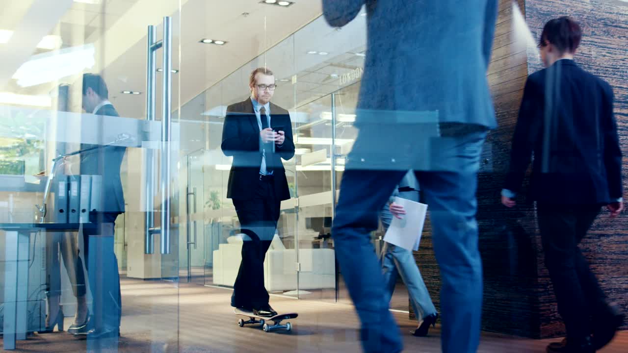 un elegante hombre de negocios usa un teléfono inteligente para montar en patineta a través del pasillo del edificio corporativo. un elegante edificio de vidrio y hormigón con una multitud multicultural de personas de negocios.