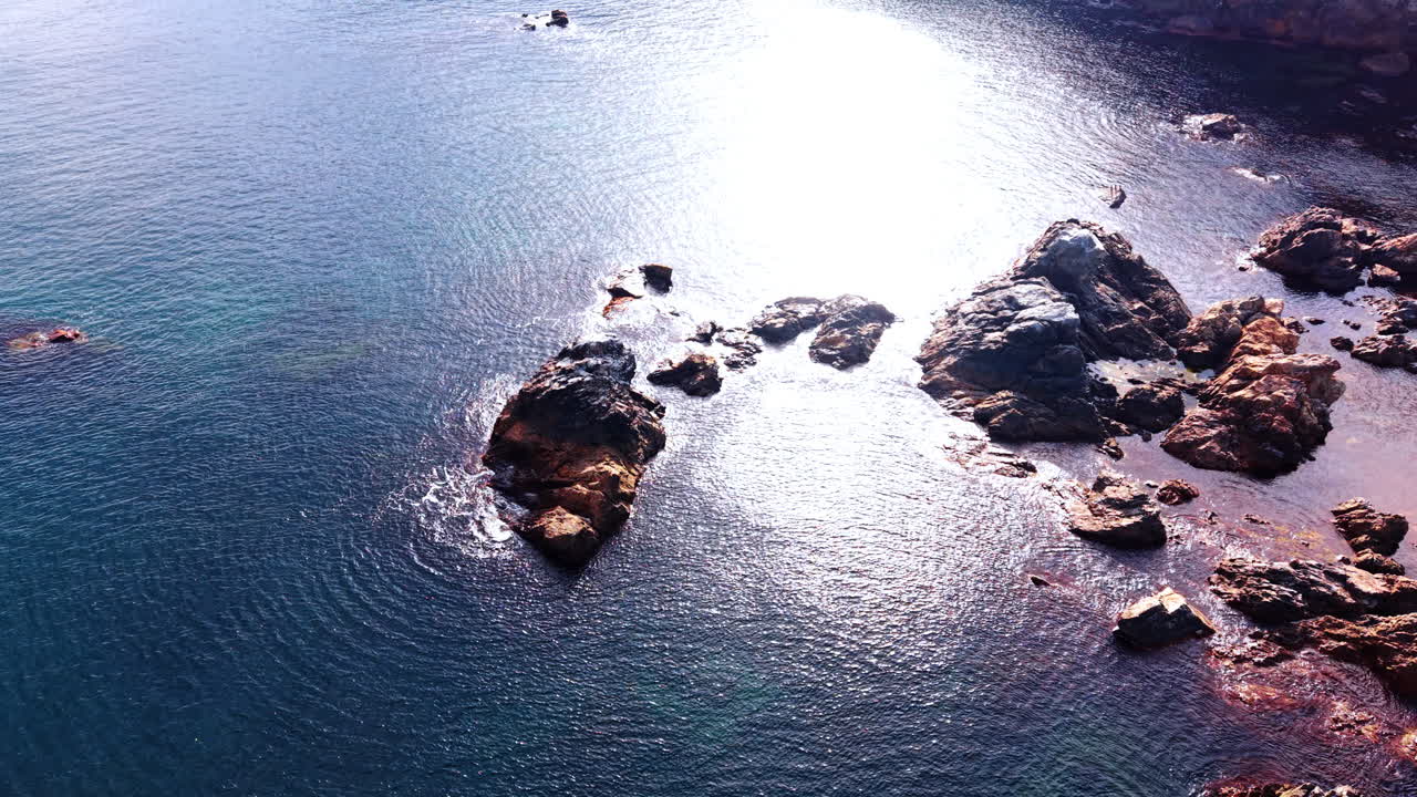 Girando intorno alle rocce che affiorano dall'acqua sulla riva. Il sole abbaglia la superficie dello specchio d'acqua.