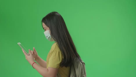 side view of asian girl student wearing a mask and use tablet while walking to school on green screen chroma key