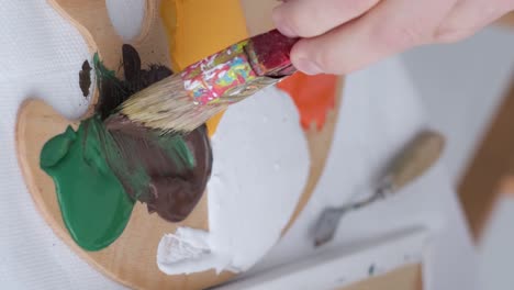 the hand of a young artist mixes paints on a palette that stands on the table the hand of a young artist mixes paints on a palette that stands on the table basic colors work with a thick paintbrush workplace of the artist