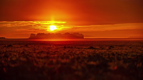 Stunning-golden-sunrise-over-a-countryside-farmland-field-with-a-copse-of-trees-in-the-hazy-distance---time-lapse