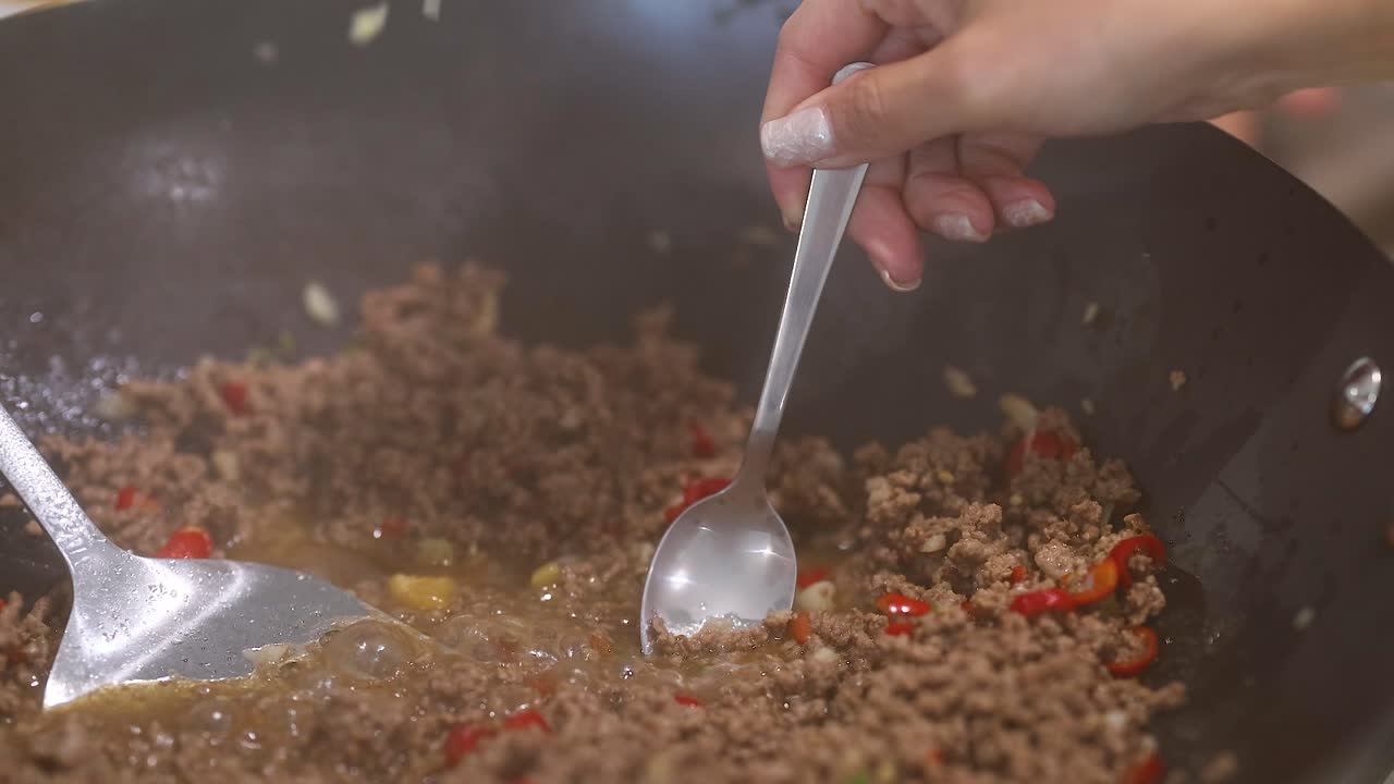 Close-up of hands stirring beef and vegetables in a pan with a spoon under bright kitchen lighting