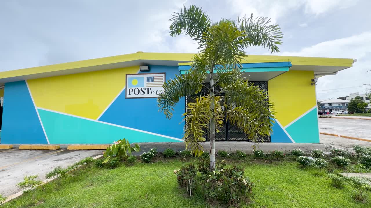 Plano geral estático de um vibrante edifício dos correios amarelo e azul sob céus nublados.
