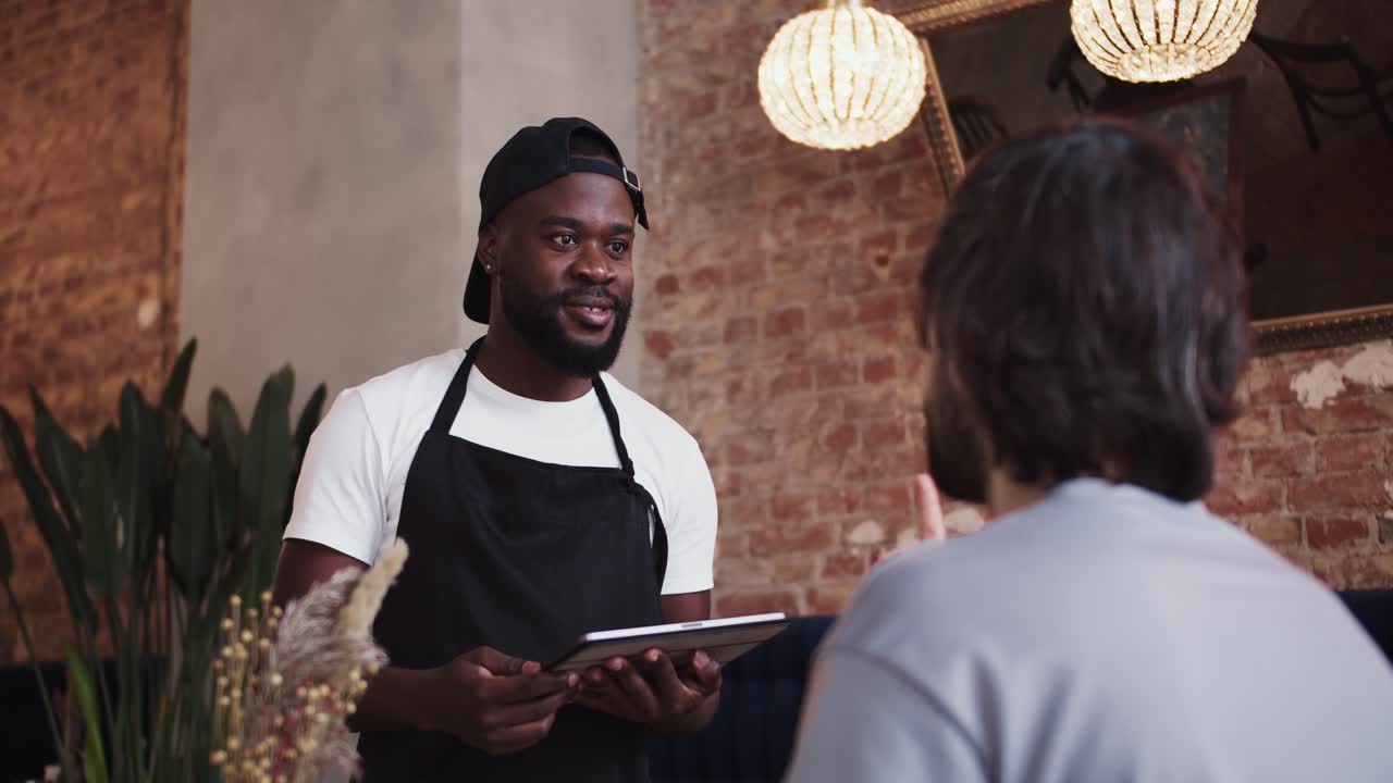 una persona negra con un delantal negro y una gorra toma un pedido de un cliente usando una tableta electrónica. video filmado en alta calidad