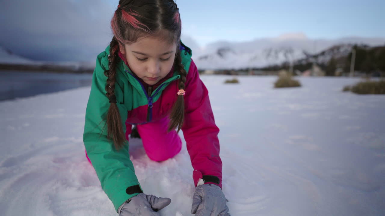 A cheerful girl plays in the snow dressed in a vibrant, warm winter suit