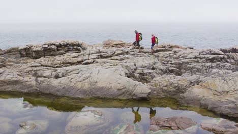 senior hiker couple with backpacks walking on the rocks while hiking near sea shore.