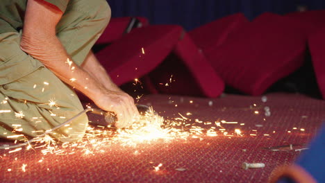 Tradesman-In-Cinema-Grinding-Bolt-And-Causing-Sparks-On-Carpet,-4K-Slow-Motion