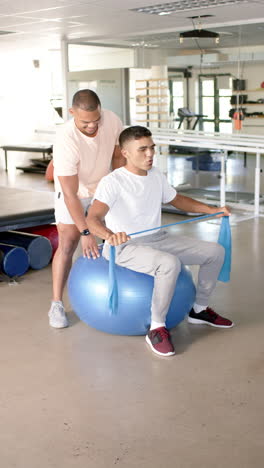 vertical video: assisting with resistance band exercises, therapist helping man on stability ball