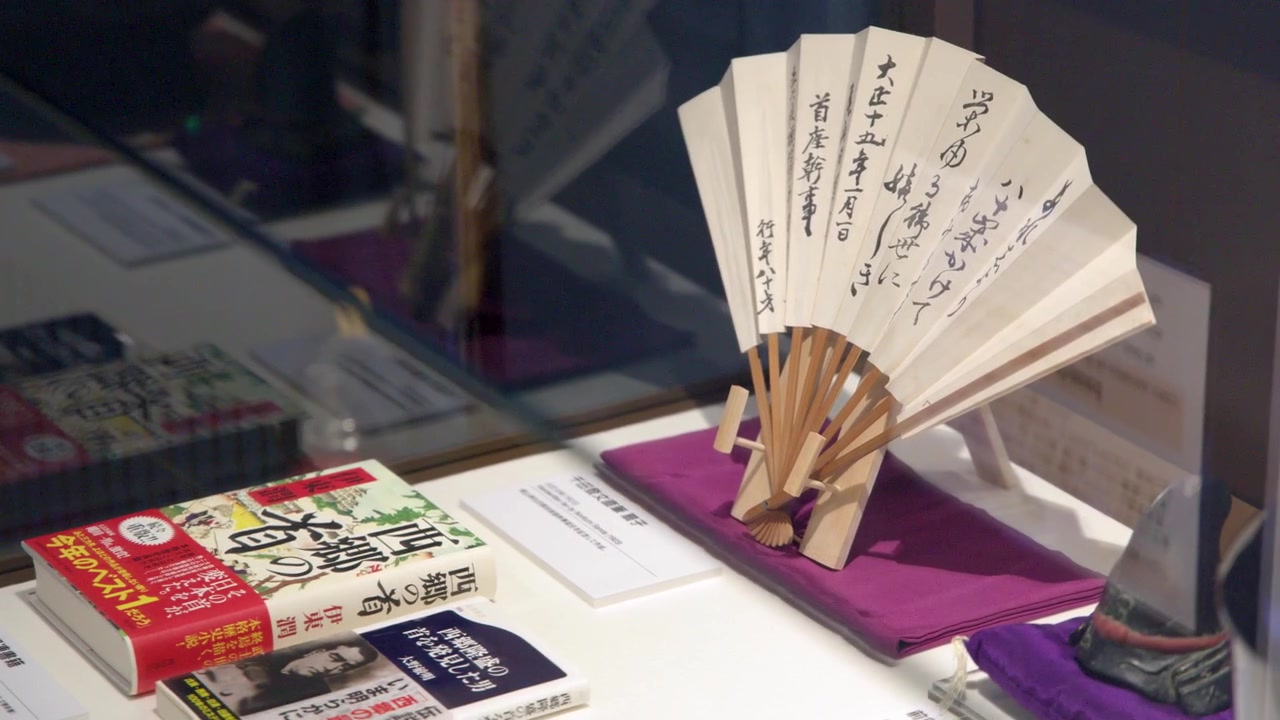 Static shot of a traditional sensu fan with ink calligraphy inside a museum display case